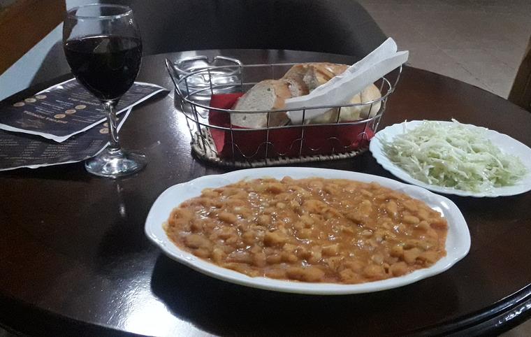 Plate of grah bean stew with shredded cabbage salad, a bread basket and a glass of red wine, Banja Luka
